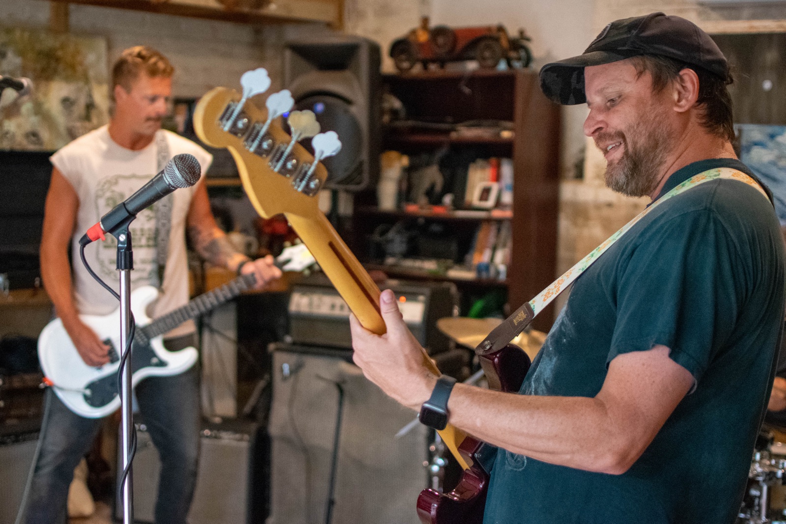 A smiling bassist playing in the foreground while another guitarist plays behind him