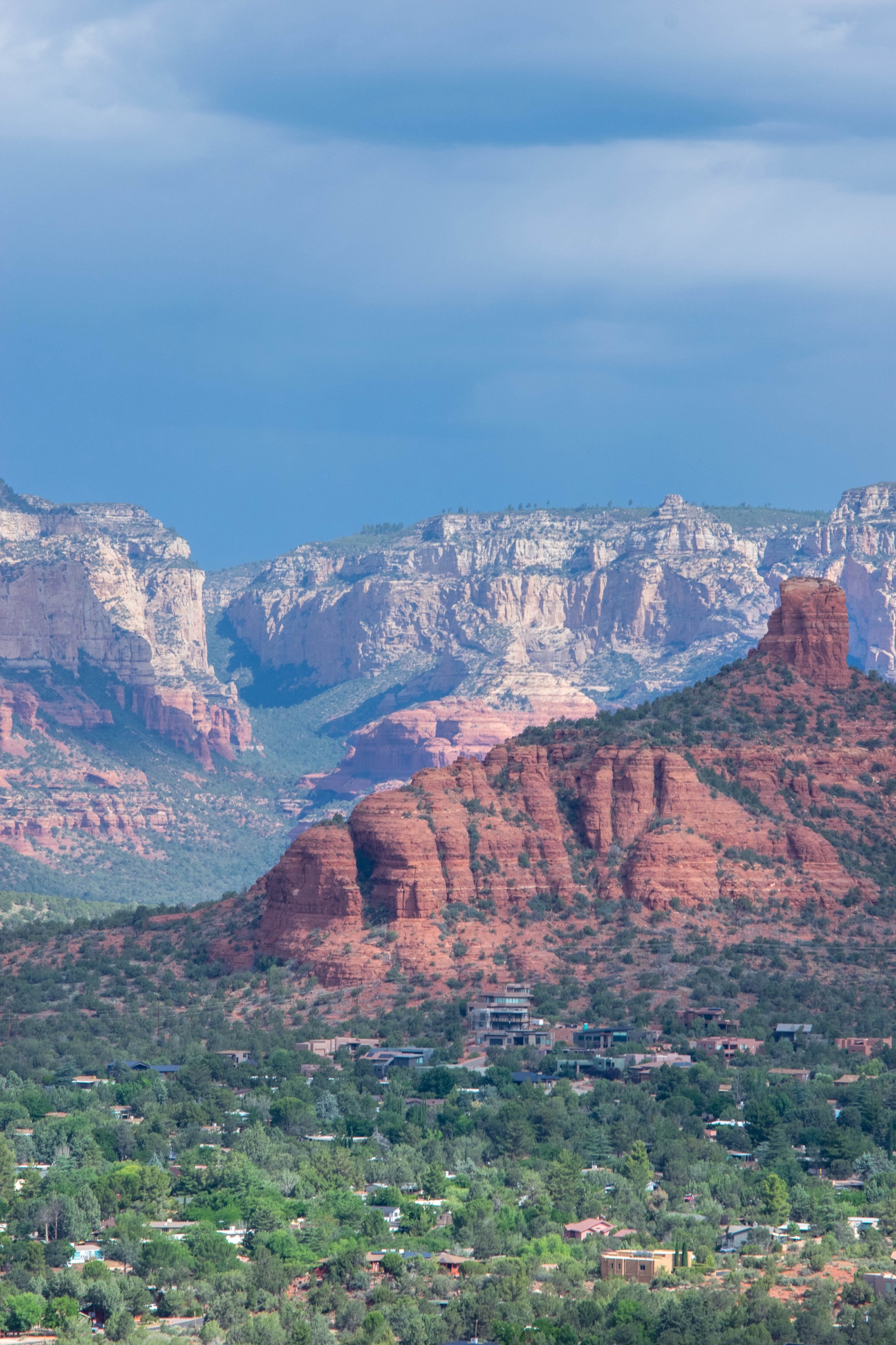 Red rock formations in front of pale canyon cliffs under a stormy blue sky